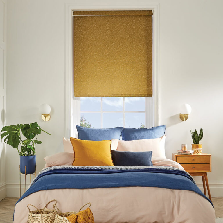 Mustard roller blind in a white bedroom, with matching and contrasting blue cushions. 